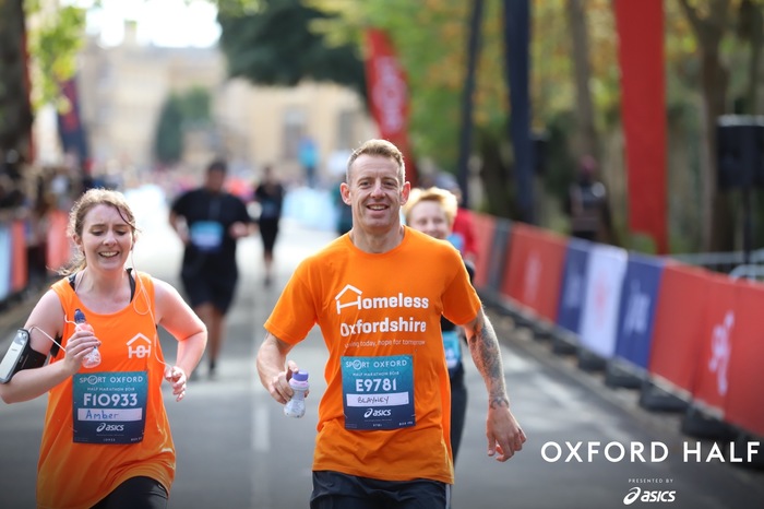 Amber and Chris cross the Oxford Half finish line. Both are wearing their Homeless Oxfordshire running vests.
